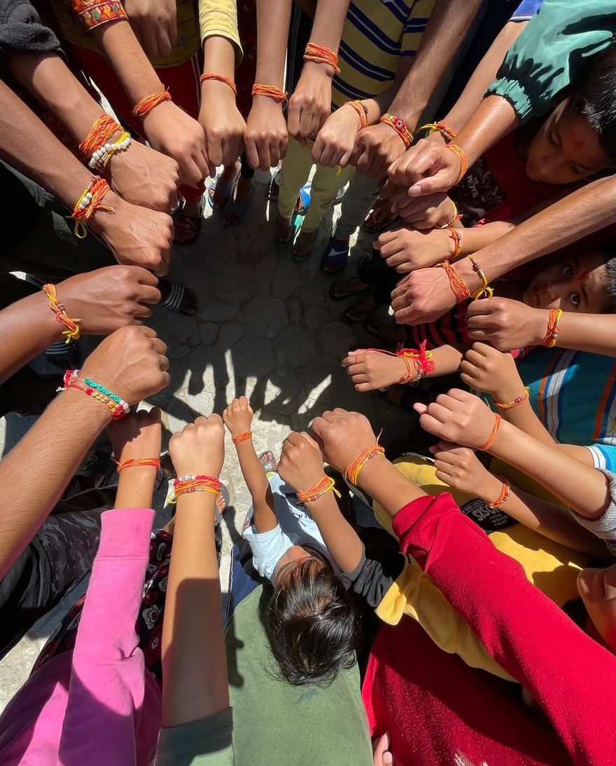 Children at the home standing in a circle with their wrists together, each wearing woven orange and yellow friendship bracelets.